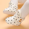 A pair of cream-colored plush baby snow boots for girls and boys with black star patterns.
