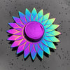 A rainbow metal fidget spinner with a smooth, iridescent purple and blue finish resting on a dark, wet surface.