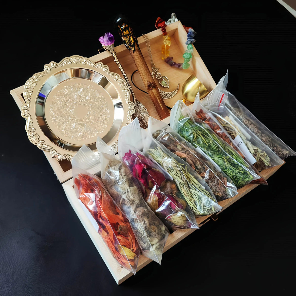 A wooden box containing a witchcraft starter kit with crystals and dried herbs, next to a decorative mirror.