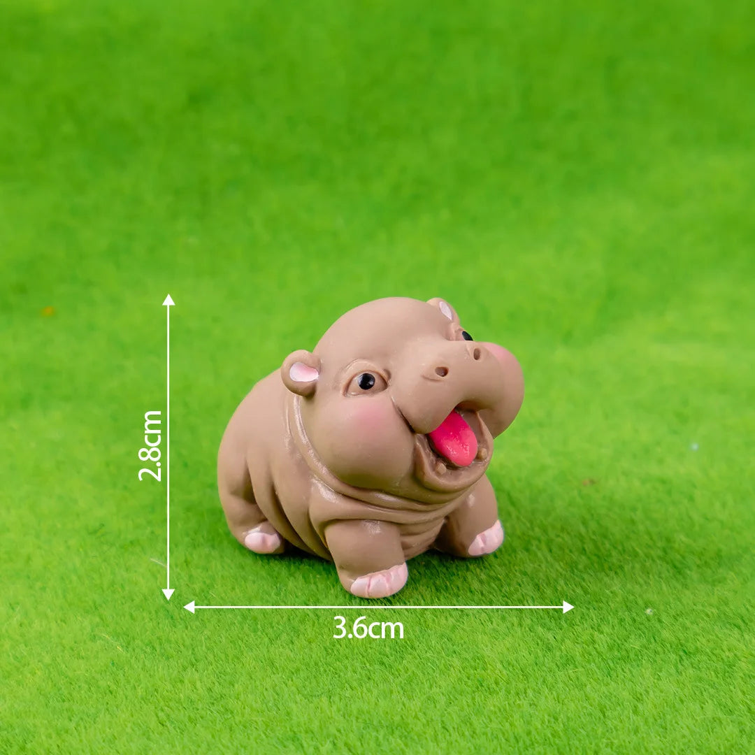 A small, light brown resin figurine of a hippo in a playful pose, photographed on green grass.