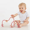 A baby is holding a pink silicone teething toy designed as a developmental aid.
