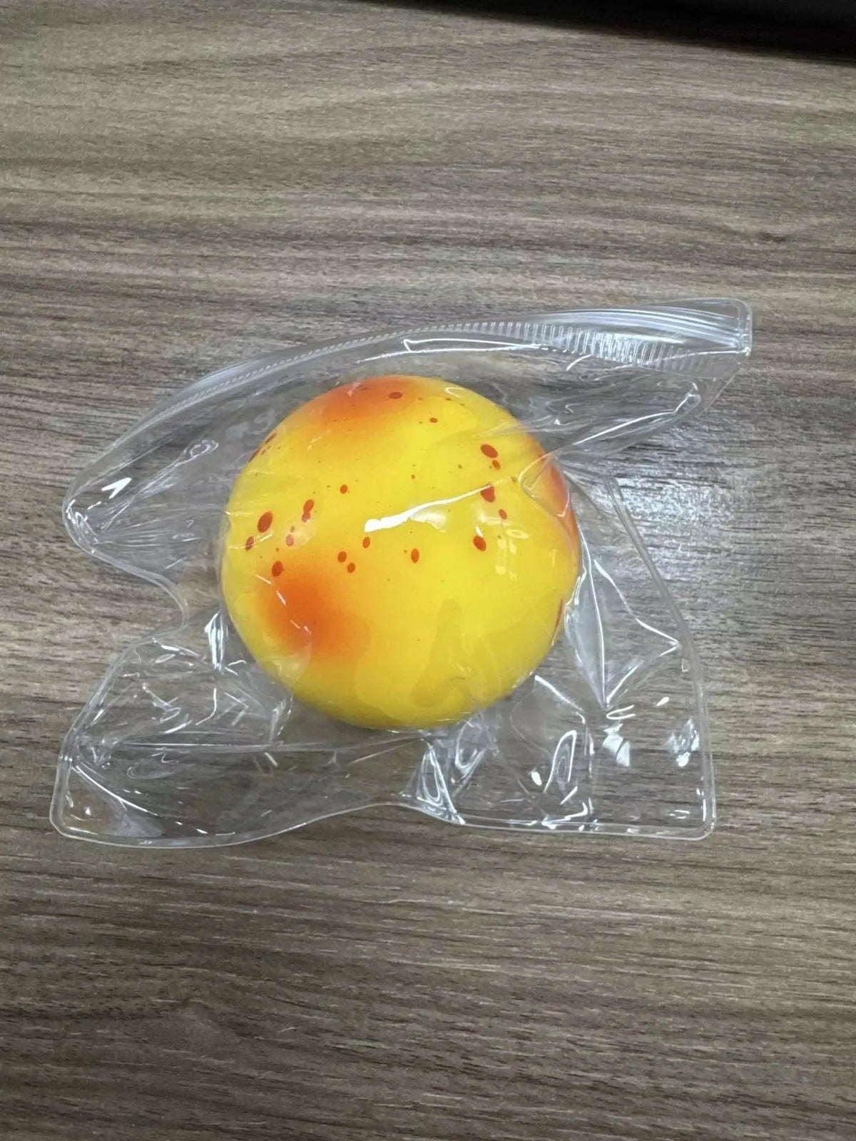 A yellow squishy potato fidget toy with orange spots is sealed in clear plastic packaging.