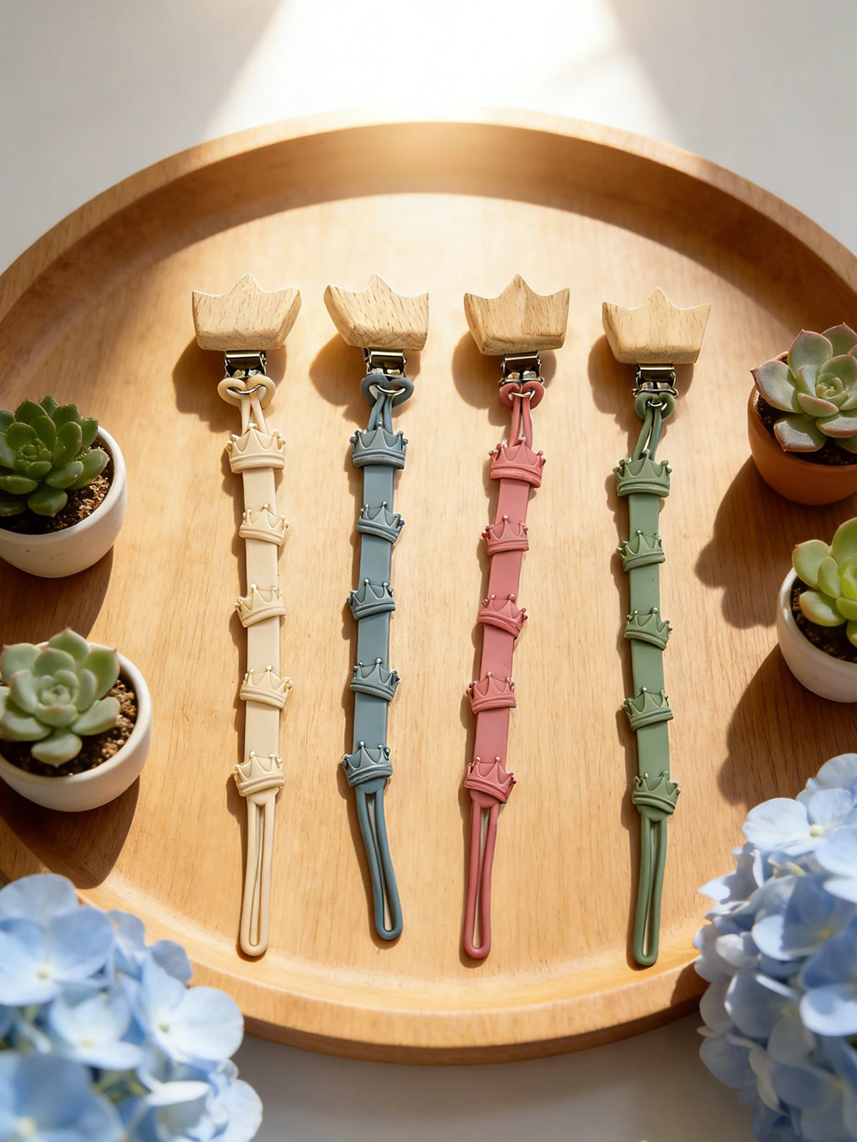 A set of baby pacifier clips with burlap flower designs arranged on a wooden tray.