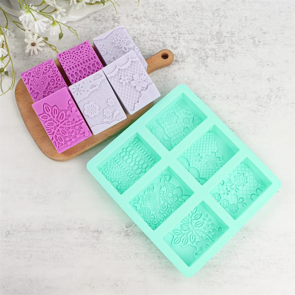 A collection of six silicone soap molds with lace patterns in various shades of purple and lilac, displayed next to a wooden 