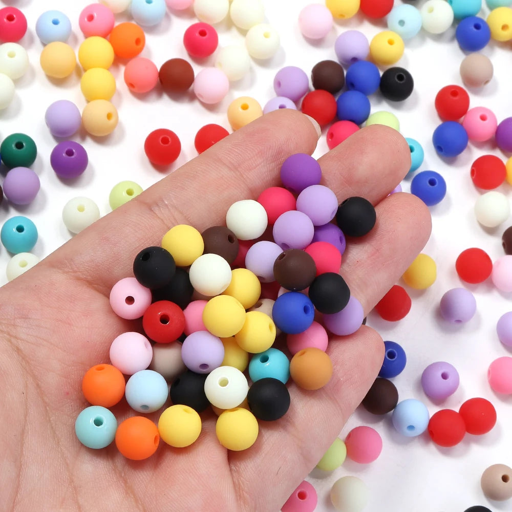 A hand holds a collection of colorful matte acrylic beads for DIY jewelry making