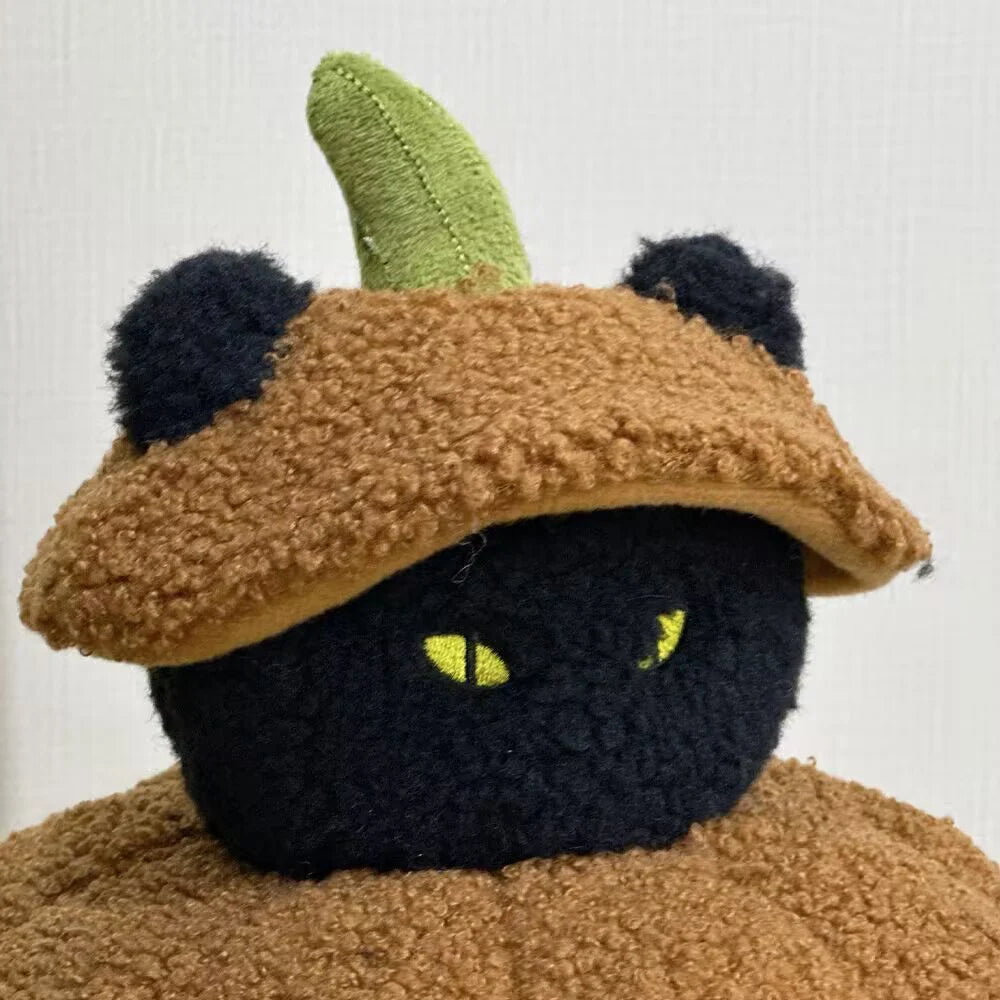 A black cat plush pillow with green ears and a brown textured body.