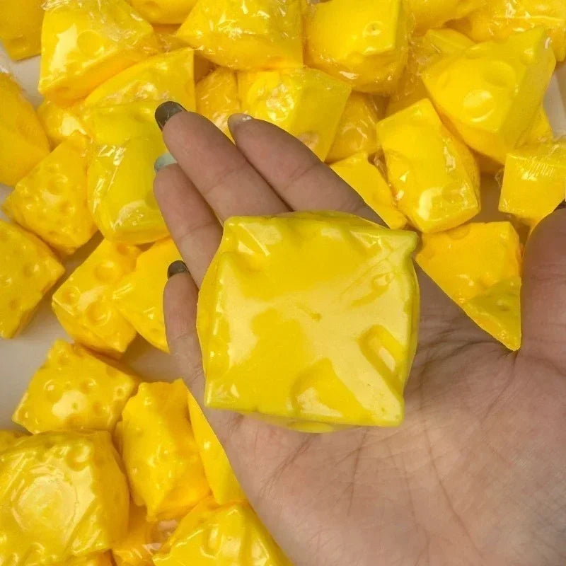 A hand holds a piece of yellow, squishy cheese ball stress relief toy surrounded by many similar pieces.
