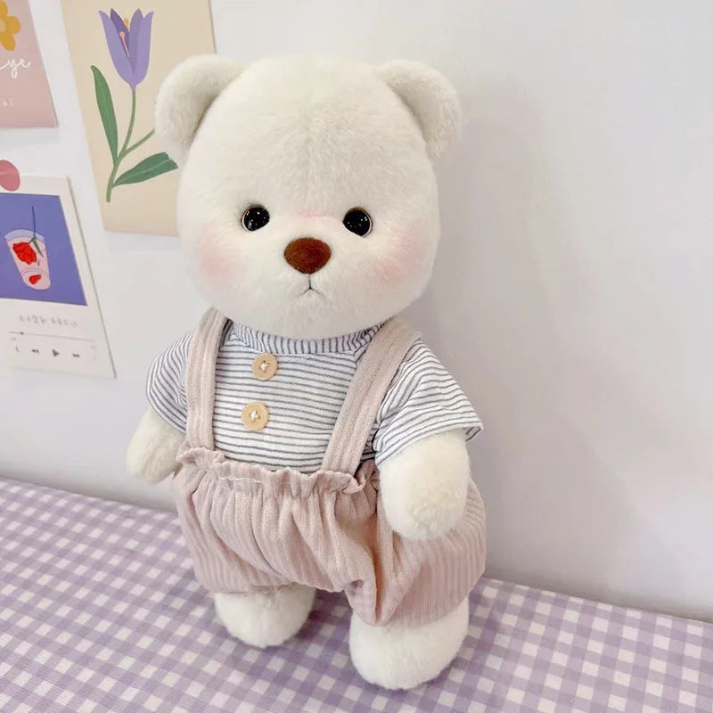 A white teddy bear plush doll wearing a striped shirt and light pink overalls.