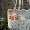A light beige crochet bag with pink mini pig keychains hanging from the strap.