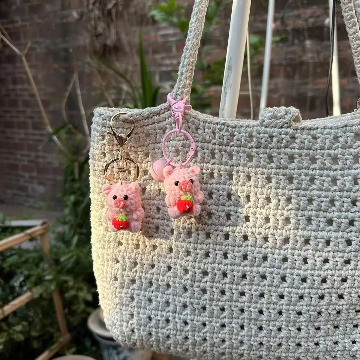 A light beige crochet bag with pink mini pig keychains hanging from the strap.