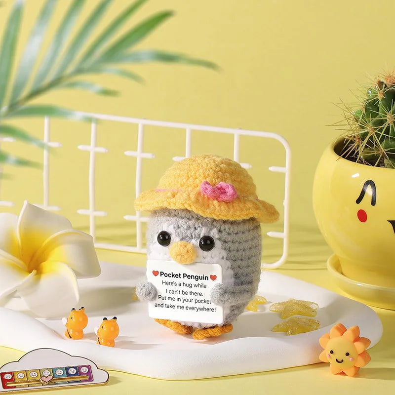 Handmade crochet penguin doll with a positive message card sitting on a white plate.
