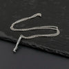 A silver chain necklace with a small metal saber keychain is displayed on a dark surface.