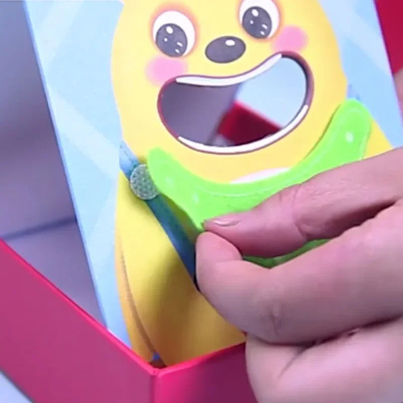 A hand is holding a yellow wooden bear feeding game toy with an open mouth, demonstrating fine motor skills.