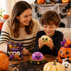 A woman and a boy are looking at a Halloween themed squishy stress relief toy on a wooden table.