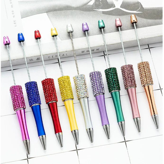 A collection of thirteen colorful ballpoint pens with various metallic and glitter finishes arranged in a row.