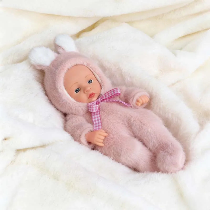 A pink fluffy reborn baby doll wearing a matching pink hooded outfit is resting on white fur.