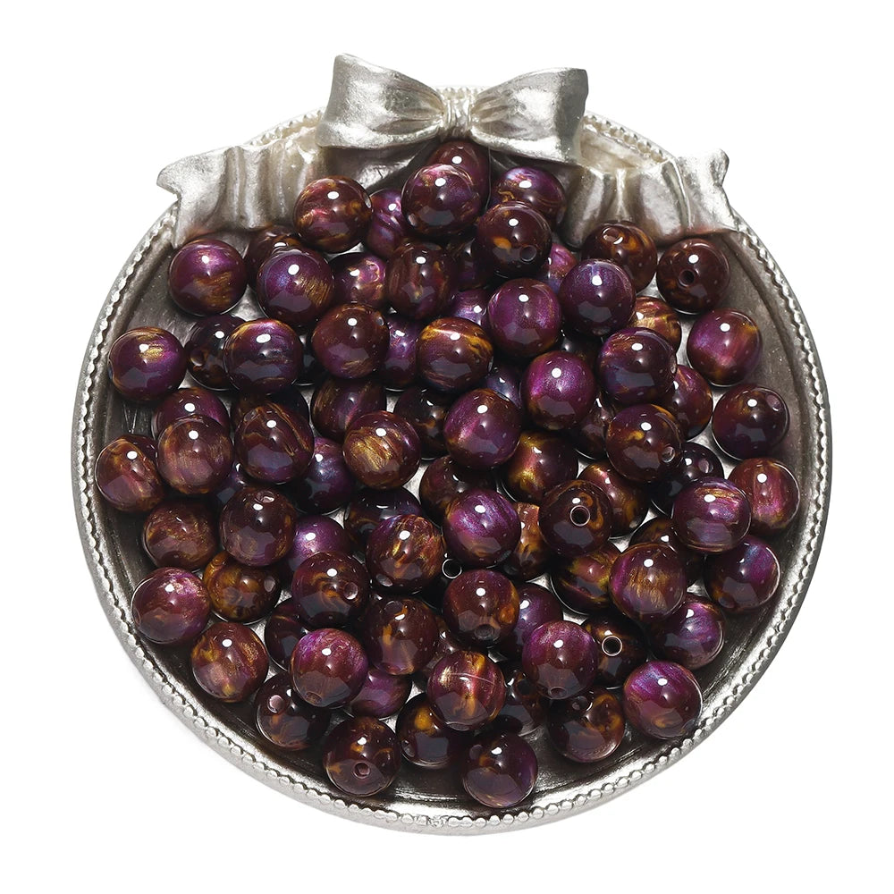 A pile of dark purple and brown glitter cat eye resin beads in a silver dish for jewelry making