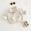 A cream fleece-lined winter coat for a toddler with a half-zip collar lying on a white surface.
