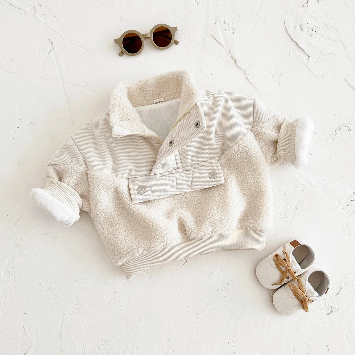 A cream fleece-lined winter coat for a toddler with a half-zip collar lying on a white surface.