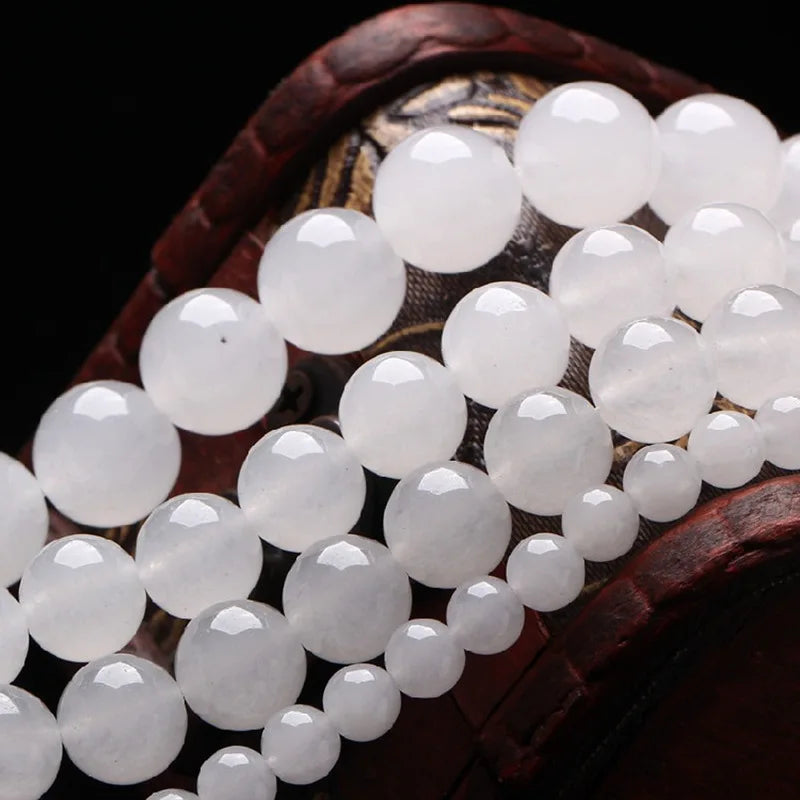A close-up of natural white crystal quartz round beads arranged on a dark wooden surface.