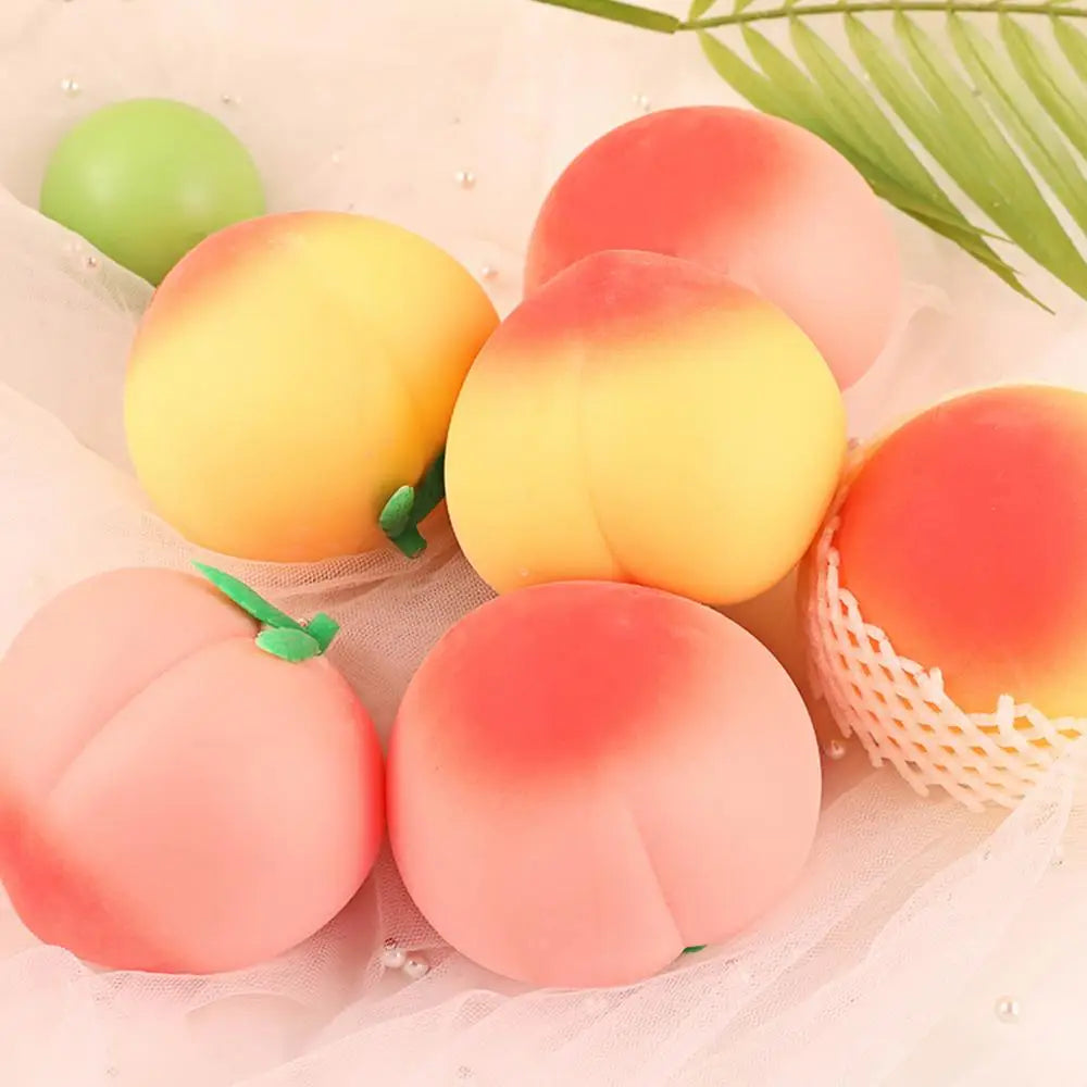 A collection of peach-shaped squeeze toys in various shades of pink and yellow resting on sheer fabric.