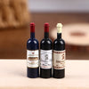 Three miniature resin wine bottles with red and white closures displayed on a wooden surface.