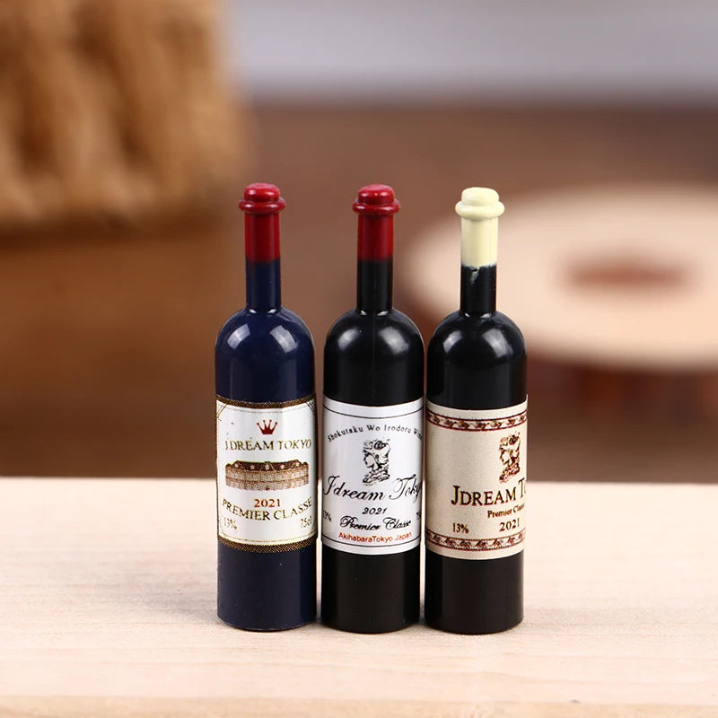 Three miniature resin wine bottles with red and white closures displayed on a wooden surface.