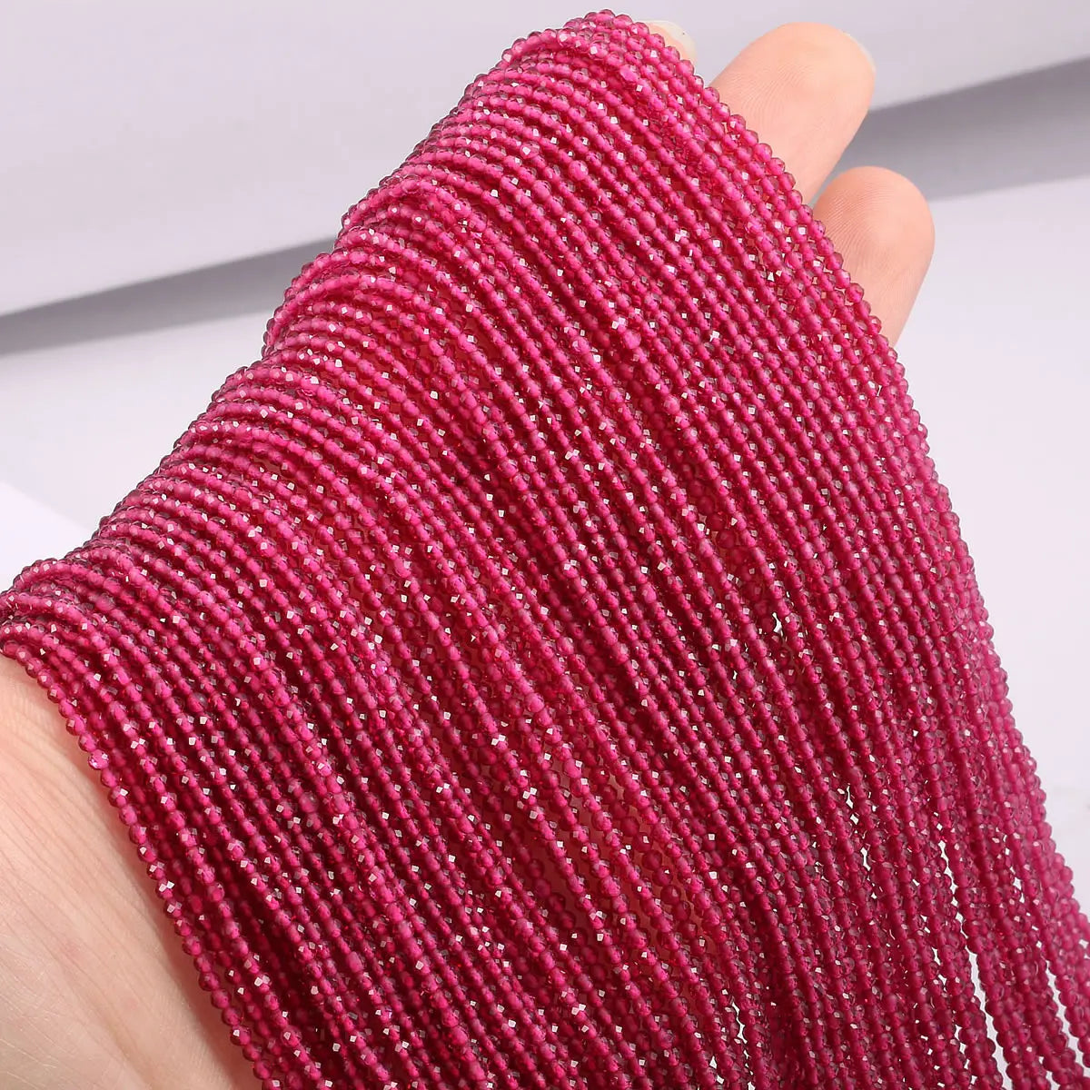 A hand is holding a strand of pink faceted natural stone beads for DIY jewelry making.
