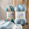 Three skeins of gradient acrylic yarn in blue, green, and gray are displayed on a wooden surface.