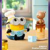 A yellow Minion figure wearing goggles is next to a brown bear collectible on a stack of pancakes.