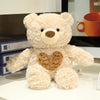 A light beige plush teddy bear sitting on a white surface in a display case.