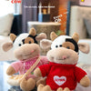 Two soft plush cow dolls dressed in sweaters, one pink and one red, displayed on a table.