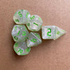 A collection of seven translucent green glitter polyhedral dice resting on a brown surface.