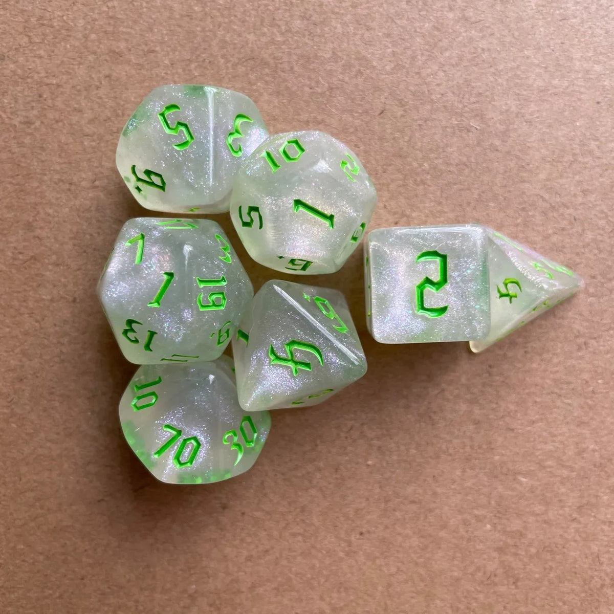 A collection of seven translucent green glitter polyhedral dice resting on a brown surface.