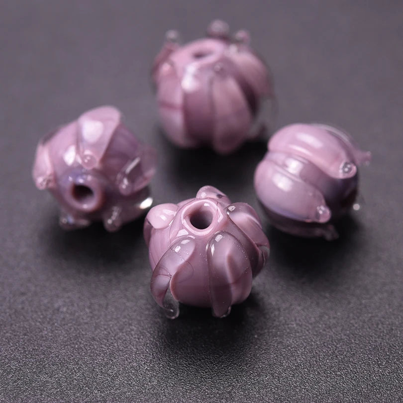 Several small, translucent purple glass charm pendants shaped like flowers are displayed on a dark surface.