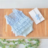 Light blue lace baby romper with ruffled trim and matching headband displayed on a wooden surface.