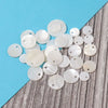 A collection of natural white shell beads in various round sizes and finishes scattered on a blue and gray surface.
