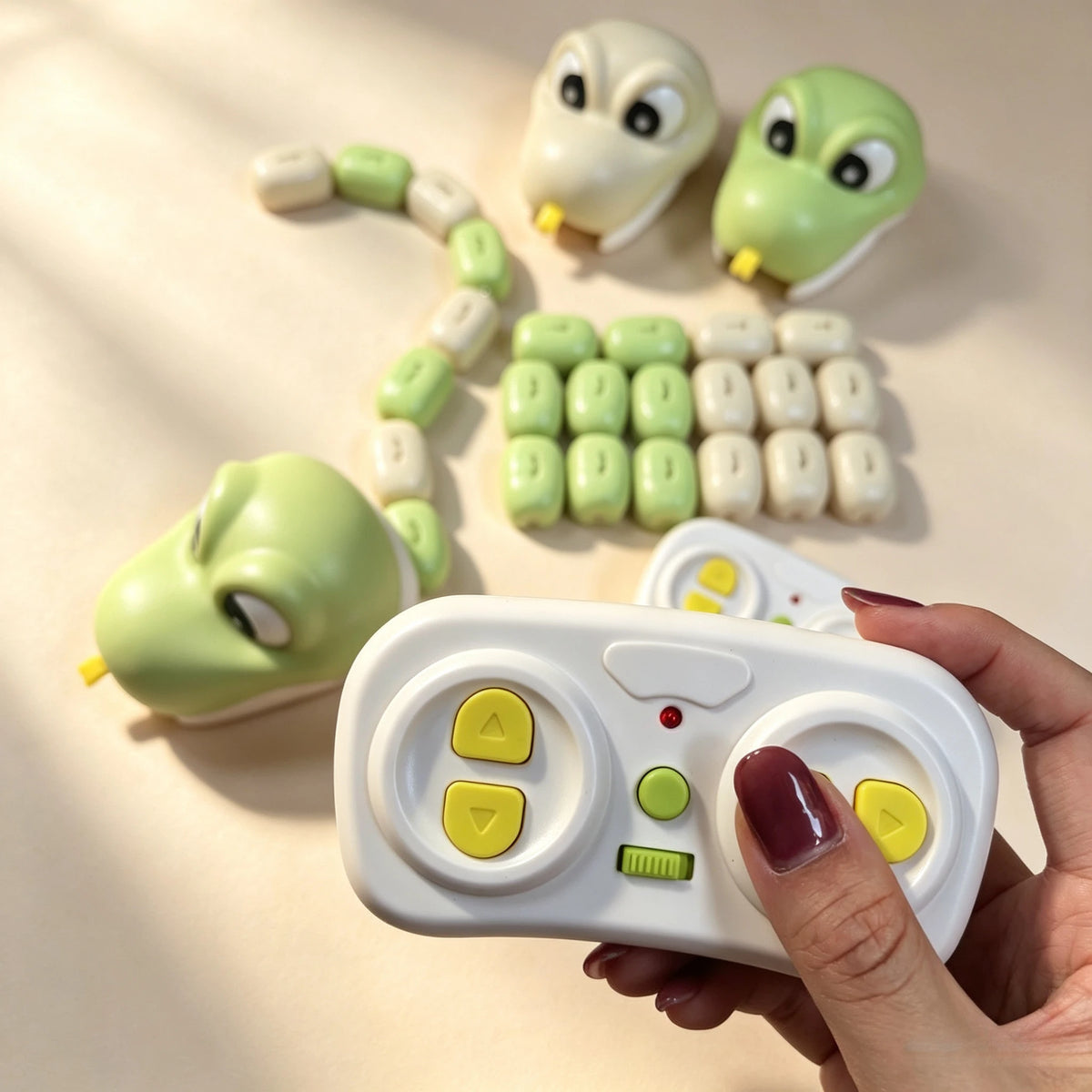 A hand holds a white remote control toy featuring green magnetic snake figures and various buttons.