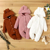 Three knitted baby rompers in terracotta, pink, and white are displayed on a wooden surface.