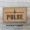 Un patch en tissu beige rectangulaire avec le mot PULSE et une ligne de battement de cœur imprimée en noir sur une surface en