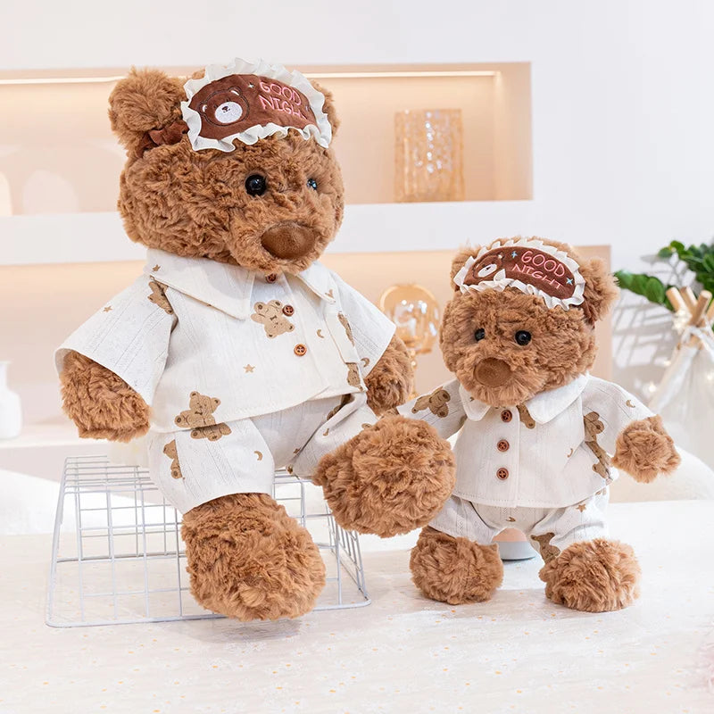 A fluffy brown teddy bear plush toy wearing a white outfit and an eye mask with a birthday cake design.