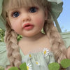 A close-up photo of a blonde toddler doll with braided hair wearing a green dress and a matching hat.