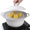 A hand is placing a silicone spill stopper lid onto a white cooking pot resting on a stovetop.