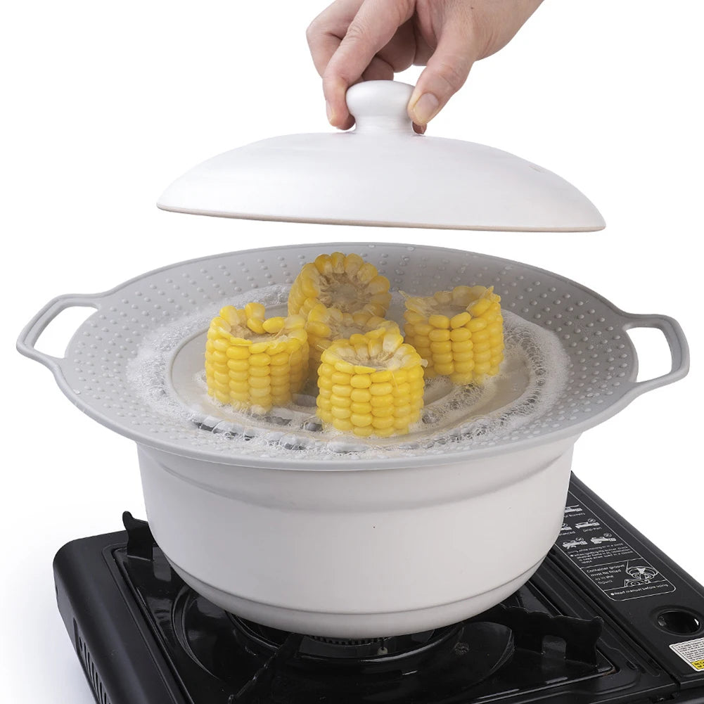 A hand is placing a silicone spill stopper lid onto a white cooking pot resting on a stovetop.