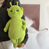 A bright lime green alien cat plush toy with large eyes and green nose, held against a dark sweater.