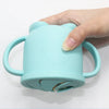 A hand is holding a light blue silicone snack cup with a lid for babies and toddlers.
