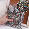 A hand holds a clear bag filled with multicolor resin nail charms for crafting.
