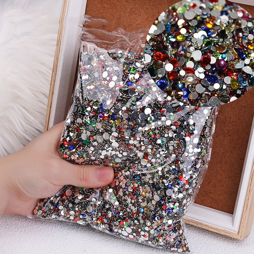 A hand holds a clear bag filled with multicolor resin nail charms for crafting.