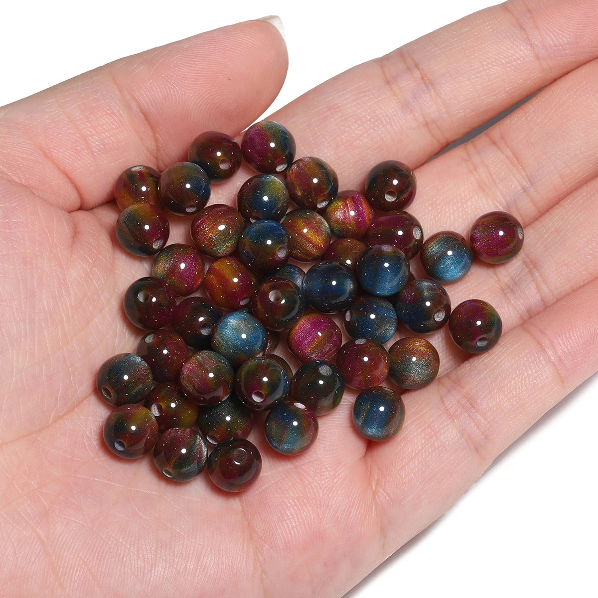 A handful of small, polished tiger eye resin beads in various shades of brown and purple resting on a hand.