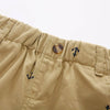 Close-up of beige cotton beach shorts featuring small navy anchor prints and a round button detail.